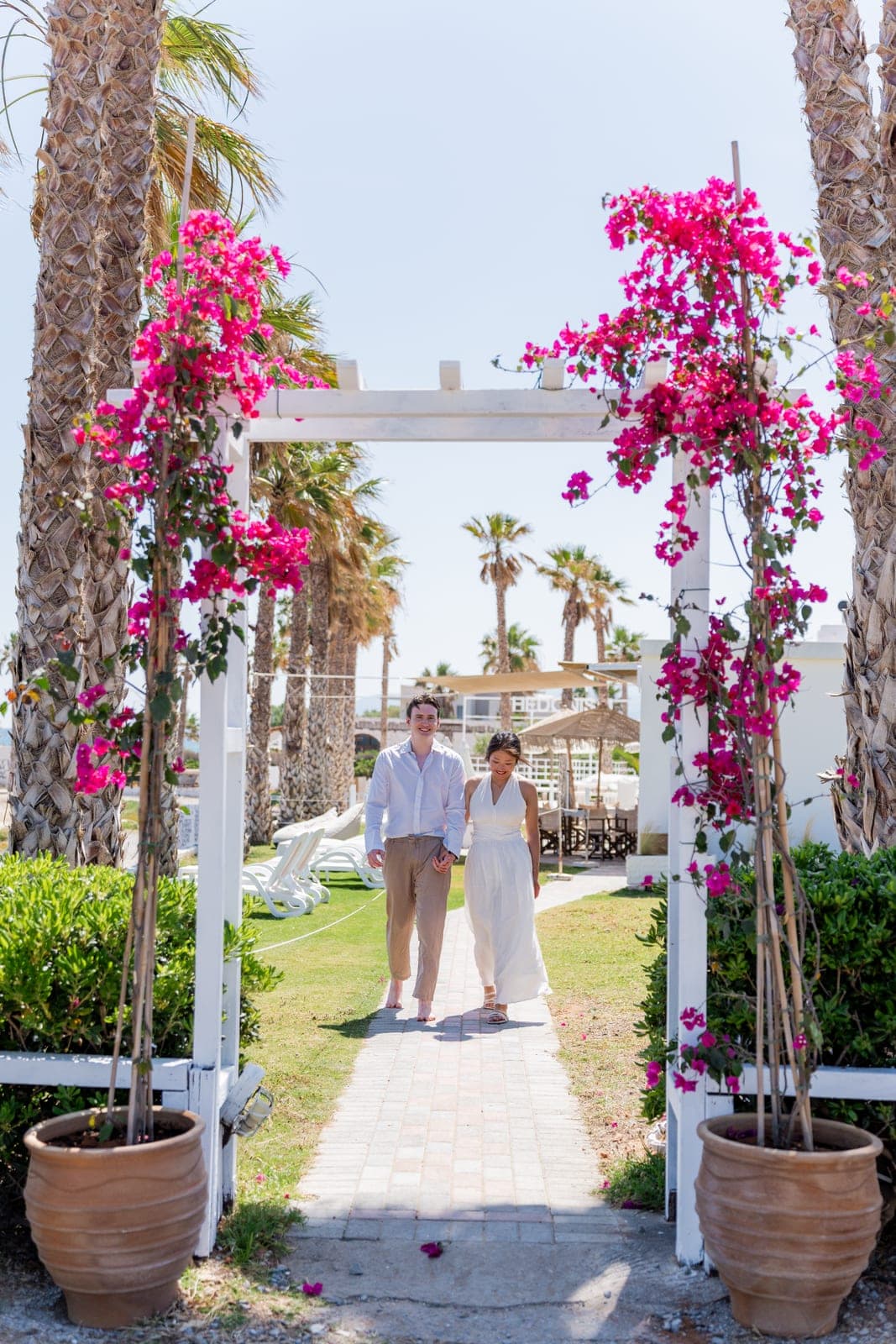 Aurélien and Yufei walking hand in hand under a bougainvillea pergola in Greece
